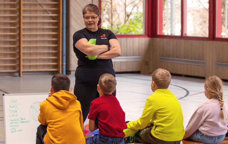 lion-kids-resilienzkurs2.jpg Die Resilienztrainerin Helen Häge spricht zu einer Gruppe von Kindern in einem Sportraum.